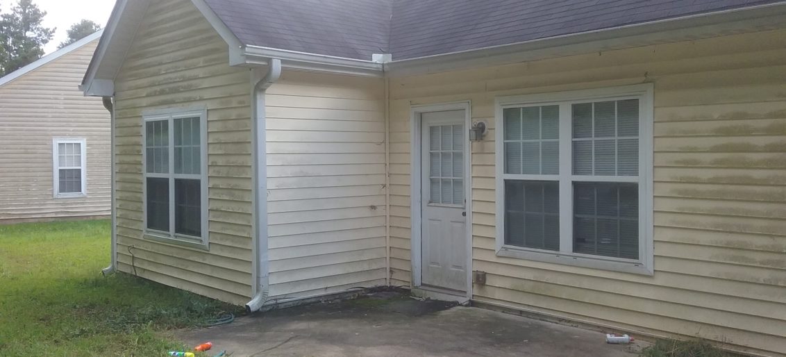 A Fairburn, GA home that needs pressure washing to remove black mildew stains on patio deck and green mildew on vinyl siding.